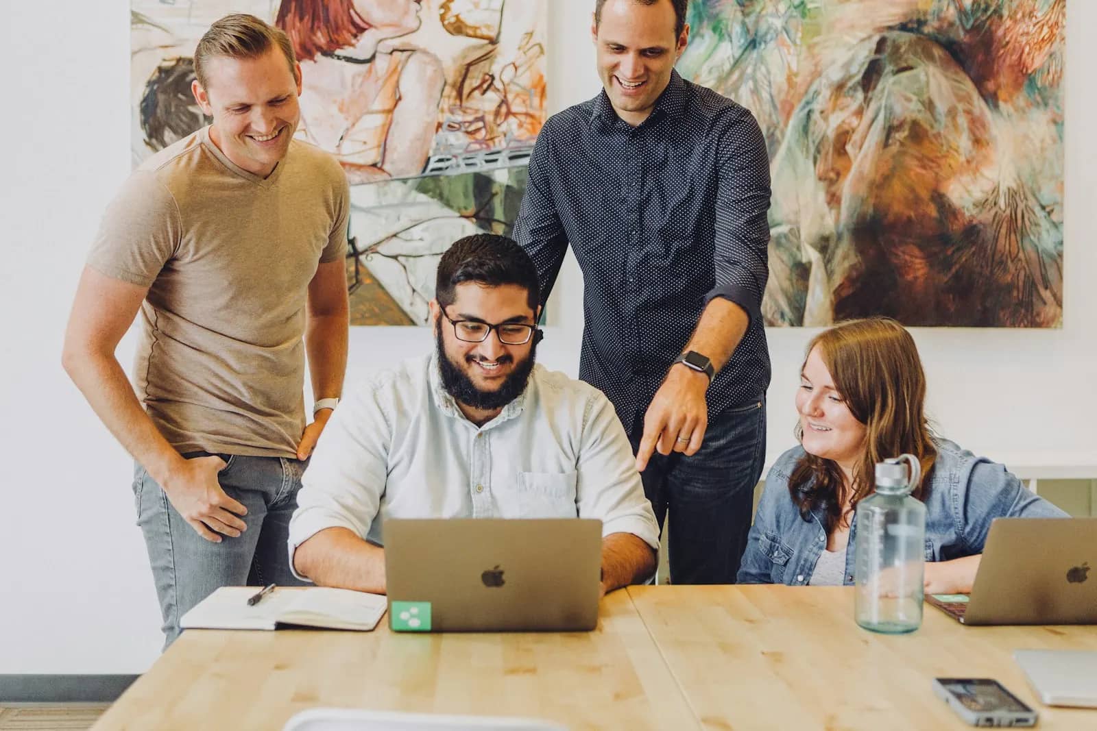 Four teammates collaborating and smiling around a laptop