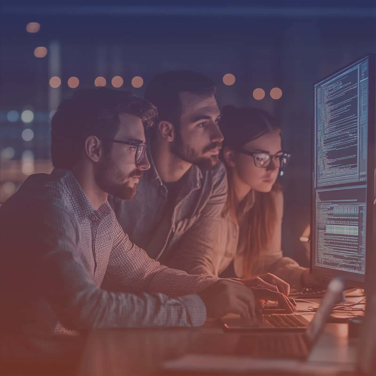 Three engineers reviewing application code together on a large monitor