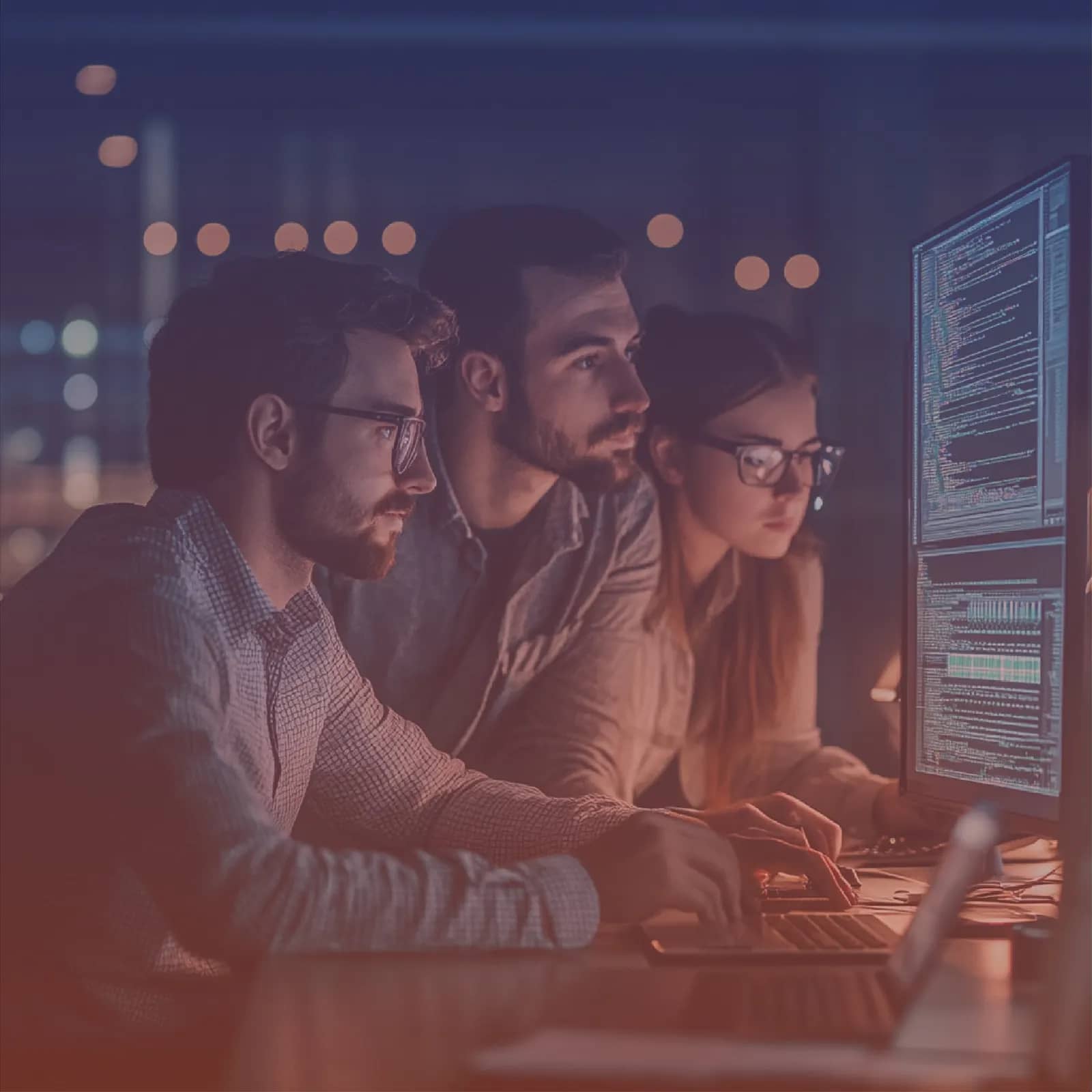 Three engineers reviewing application code together on a large monitor